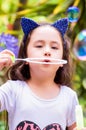 Happy little girl playing with soap bubbles on a summer nature, wearing a blue ears tiger accessories over her head in a Royalty Free Stock Photo