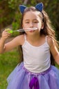 Happy little girl playing with soap bubbles on a summer nature, wearing a blue ears tiger accessories over her head and Royalty Free Stock Photo