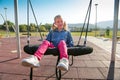 Happy little girl playing on a swing and having fun at kids modern playground Royalty Free Stock Photo