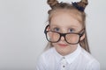 Happy little girl portrait, wearing white blouse and black frame eyeglasses, standing against white wooden background. Back to sch Royalty Free Stock Photo