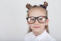 Happy little girl portrait, wearing white blouse and black frame eyeglasses, standing against white wooden background. Back to sch Royalty Free Stock Photo