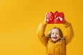 Happy little girl preschooler in a winter jacket is holding a box with a gift over the head. Royalty Free Stock Photo