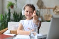 Happy little girl pupil study online using laptop at home, smiling small child show thumb up recommend class or lesson Royalty Free Stock Photo