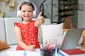 Happy little girl pupil study online using laptop at home, smiling small child show thumb up recommend class or lesson Royalty Free Stock Photo