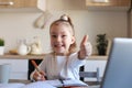 Happy little girl pupil study online using laptop at home, smiling small child show thumb up recommend class or lesson Royalty Free Stock Photo