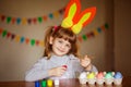 Happy little girl with rabbit ears painting eggs