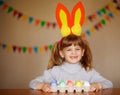 Happy little girl with rabbit ears painting eggs