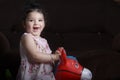 Happy Little girl riding a plastic red donkey at home