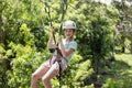 Happy little girl riding a zip line in a lush tropical forest