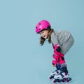 Happy little girl in roller skates with pink protective gear over blue