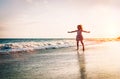 Happy little girl running inside water spreading her hands up on the beach - Baby having fun making splashing in the sea