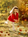 A happy little girl runs in the park with autumn leaves in a bright red coat and gray knitted skirt. Childhood. Active children.