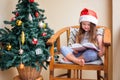 Happy little girl in the santa hat reads a book near christmas tree Royalty Free Stock Photo