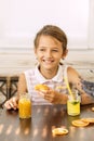 Happy little girl of school age enjoying healthy breakfast eating sandwich and fruits and drinking orange juice sitting