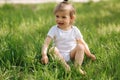 Happy little girl sits on the grass outdoors. Cute baby girl in white bodysuit and sunglasses on the backyard. Adorable Royalty Free Stock Photo