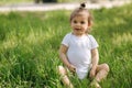 Happy little girl sits on the grass outdoors. Cute baby girl in white bodysuit and sunglasses on the backyard. Adorable Royalty Free Stock Photo