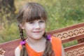 Happy little girl sits on wooden beanch at sunny summer d