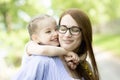 Happy little girl sitting on her mom shoulders or back on a sunny summer day and kissing her mother cheek Royalty Free Stock Photo