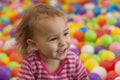 Happy little girl sitting in multi-colored plastic balls. Beautiful curly cheerful bright child on a background of