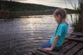 Girl sits on pontoon bridge at lake and enjoys warm sunny evening, happy summertime, countryside Royalty Free Stock Photo