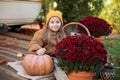 Happy little girl sitting on porch of house with chrysanthemums potted and pumpkins. home fall decoration for Halloween or Thanksg Royalty Free Stock Photo