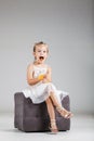 Happy little girl sitting on a stool in studio, eating crisps