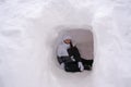 Happy little girl in ski suit sitting inside white snow mountain at winter resort during leisure games travel Royalty Free Stock Photo