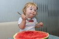 One-year-old girl eats watermelon with a spoon, the first independent use of vitamins, sweet berry Royalty Free Stock Photo