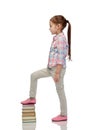 Happy little girl stepping on book pile