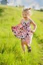A happy little girl in summer dress with pigtails run in a green field, light of warm rays of the sun Royalty Free Stock Photo
