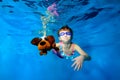 Happy little girl swims underwater in the pool, holding a toy dog in hand, looking at camera and smiling. Portrait. Royalty Free Stock Photo