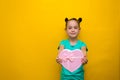 Happy little girl with tails standing isolated over yellow background holding shopping pink bag. smiles thoughtfully Royalty Free Stock Photo