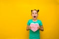 Happy little girl with tails standing isolated over yellow background holding shopping pink bag in surprise Royalty Free Stock Photo