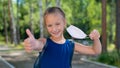 Happy little girl takes off the mask and shows thumb outdoors. Joyful smiling schoolgirl with a backpack pushes the mask