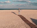 Happy little girl walking alone on wooden boardwalk on seascape background blue sky. Child resting running on sand beach Royalty Free Stock Photo