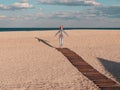 Happy little girl walking alone on wooden boardwalk on seascape background blue sky. Child resting running on sand beach Royalty Free Stock Photo