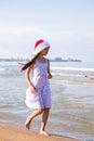 Happy little girl wearing a red Santa hat running through the sea water on clear sunny day Royalty Free Stock Photo