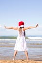 Happy little girl wearing a red Santa hat standing arms outstretched on the s Royalty Free Stock Photo