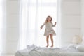 Happy little girl wearing white pajamas jumping on bed in white bedroom Royalty Free Stock Photo