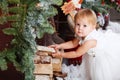 Happy little girl in white dress puts firewood in the Christmas wooden brown decorated room interior Royalty Free Stock Photo