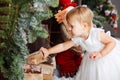 Happy little girl in white dress puts firewood in the Christmas wooden brown decorated room interior Royalty Free Stock Photo