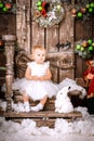 Happy little girl in white dress sitting in the Christmas wooden brown decorated room interior Royalty Free Stock Photo