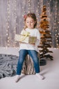 Happy little girl in a white sweater and blue jeans posing near christmas tree Royalty Free Stock Photo