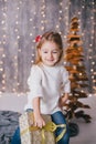 Happy little girl in a white sweater and blue jeans posing near christmas tree Royalty Free Stock Photo