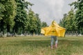 Happy little girl in yellow raincoat and muddy rubber boots running on dirt road through green grass near blooming rape seed field Royalty Free Stock Photo