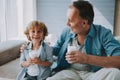 Happy little grandson drinks milk with straw in glass with grandfather. Royalty Free Stock Photo