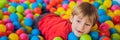 Happy little kid boy playing at colorful plastic balls playground high view. Adorable child having fun indoors BANNER