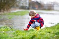 Happy little kid boy in yellow rain boots playing with paper ship boat by huge puddle on spring or autumn day. Active Royalty Free Stock Photo