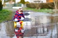 Happy little kid boy in yellow rain boots playing with paper ship boat by huge puddle on spring or autumn day Royalty Free Stock Photo