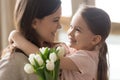 Happy kid daughter embracing mom receiving tulips on mothers day